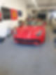 A vibrant red sports car sits in a garage, surrounded by tools and tires