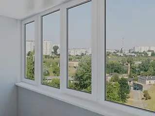 Four large windows overlook a cityscape with green trees and tall buildings under a clear blue sky