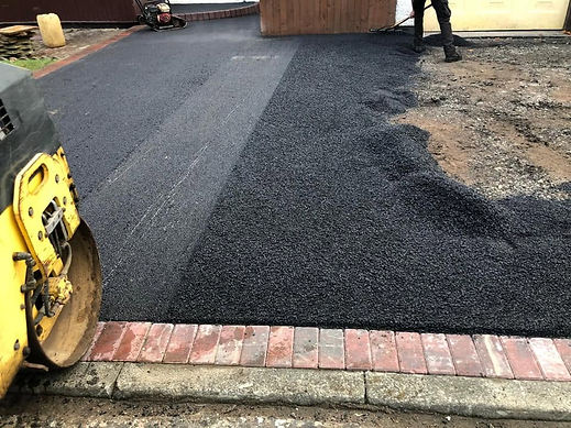 Yellow ride on compaction roller machine smoothing out a fresh layer of hot black tarmac road surfacing