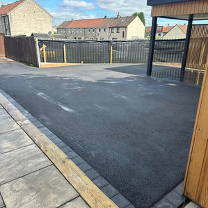 Newly laid black tarmac driveway with stone block paving borders next to a wooden fence