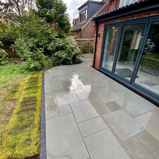 Wet patio with large grey tiles next to a brick house with glass doors