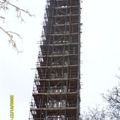 A tall structure under renovation, covered in dense scaffolding against a cloudy sky