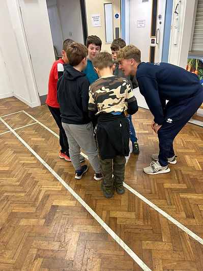 A group of seven boys huddled closely in a circle indoors, appearing engaged and focused