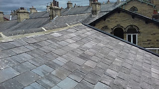 Rooftop view showing grey slate tiles, with older brick buildings and chimneys in the background