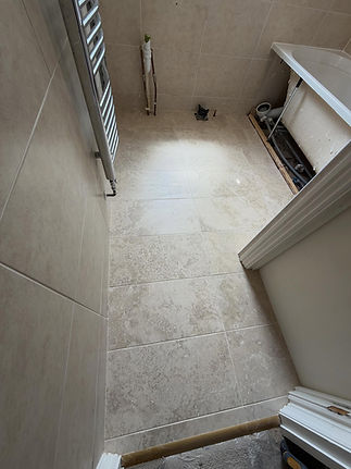 Narrow bathroom with beige tile flooring and partially installed heater