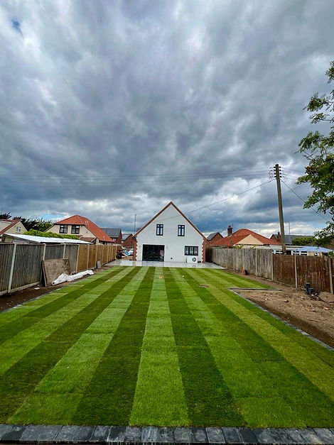 Expansive lawn with striped grass leads to a white house under a dramatic cloudy sky