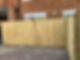 A newly installed wooden fence stands in front of a brick house with white-framed windows