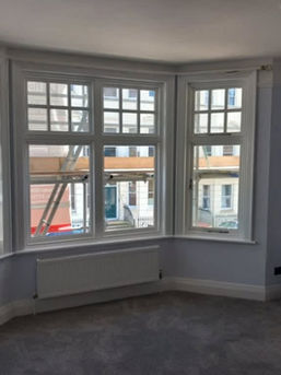 A bright, unfurnished room features a large bay window with white frames, gray carpet