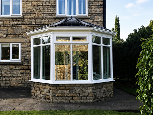 A modern conservatory with large glass windows and white frames extends from a stone house