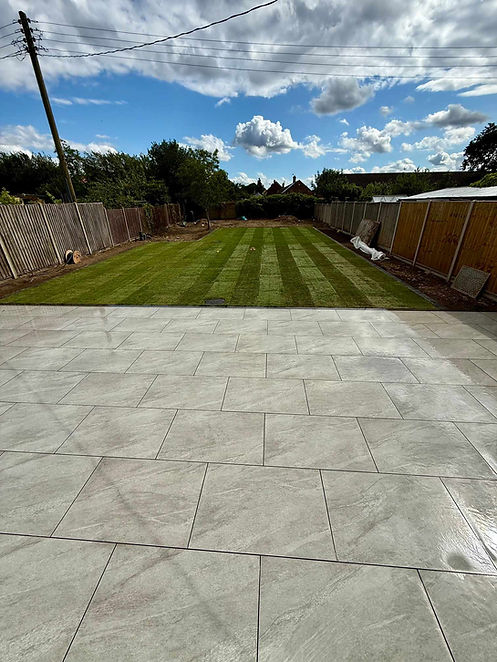 Freshly laid patio with light gray tiles in the foreground, leading to a neatly mowed lawn