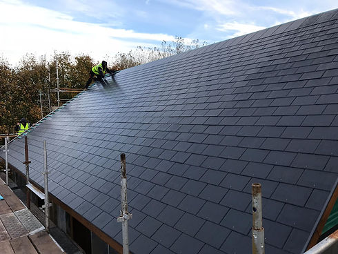 A worker in a high-visibility vest installs slate tiles on a large, sloped roof