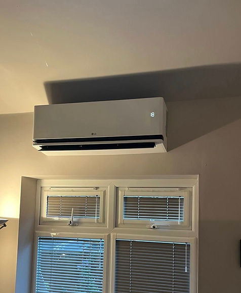 A white wall-mounted air conditioner is positioned above two windows with closed blinds