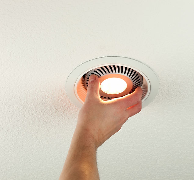 A hand is adjusting a glowing recessed ceiling light embedded in a textured white ceiling