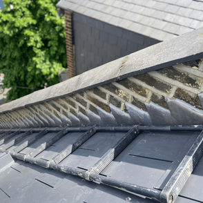 Close-up of a slate rooftop with a brick wall running along the edge