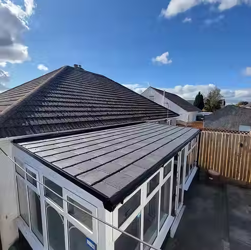 A modern conservatory with a sleek, flat, paneled roof attached to a brick house