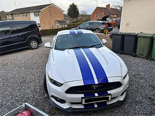 Front angle of a white Ford Mustang with blue racing stripes parked in a driveway