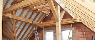Timber roof framework under construction with brickwork and ladder visible