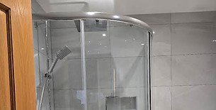 Corner glass shower enclosure with a chrome shower head and curved sliding doors