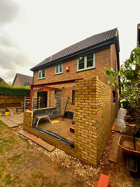 Two-story brick house under renovation, with a new extension featuring incomplete brick walls and exposed steel beams