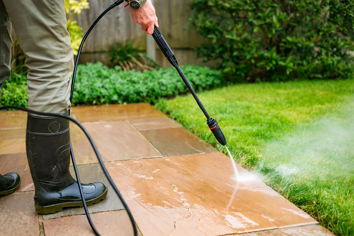 Person cleaning a patio with a pressure washer, wearing boots