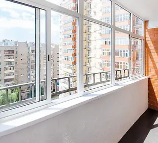 Modern enclosed balcony with large glass windows overlooking high-rise apartments