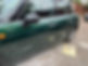 A green car with a noticeable dent in the right rear door is parked on a brick driveway
