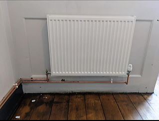 White radiator mounted on a wall with exposed copper pipes