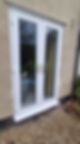 White double French doors with reflective glass and gold handles stand on a textured beige wall