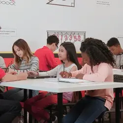 Group of school children sitting around a classroom table working on activities with a tutor