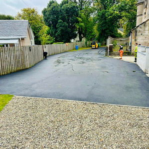 Long tarmac driveway and path running alongside a stone wall and gravel area