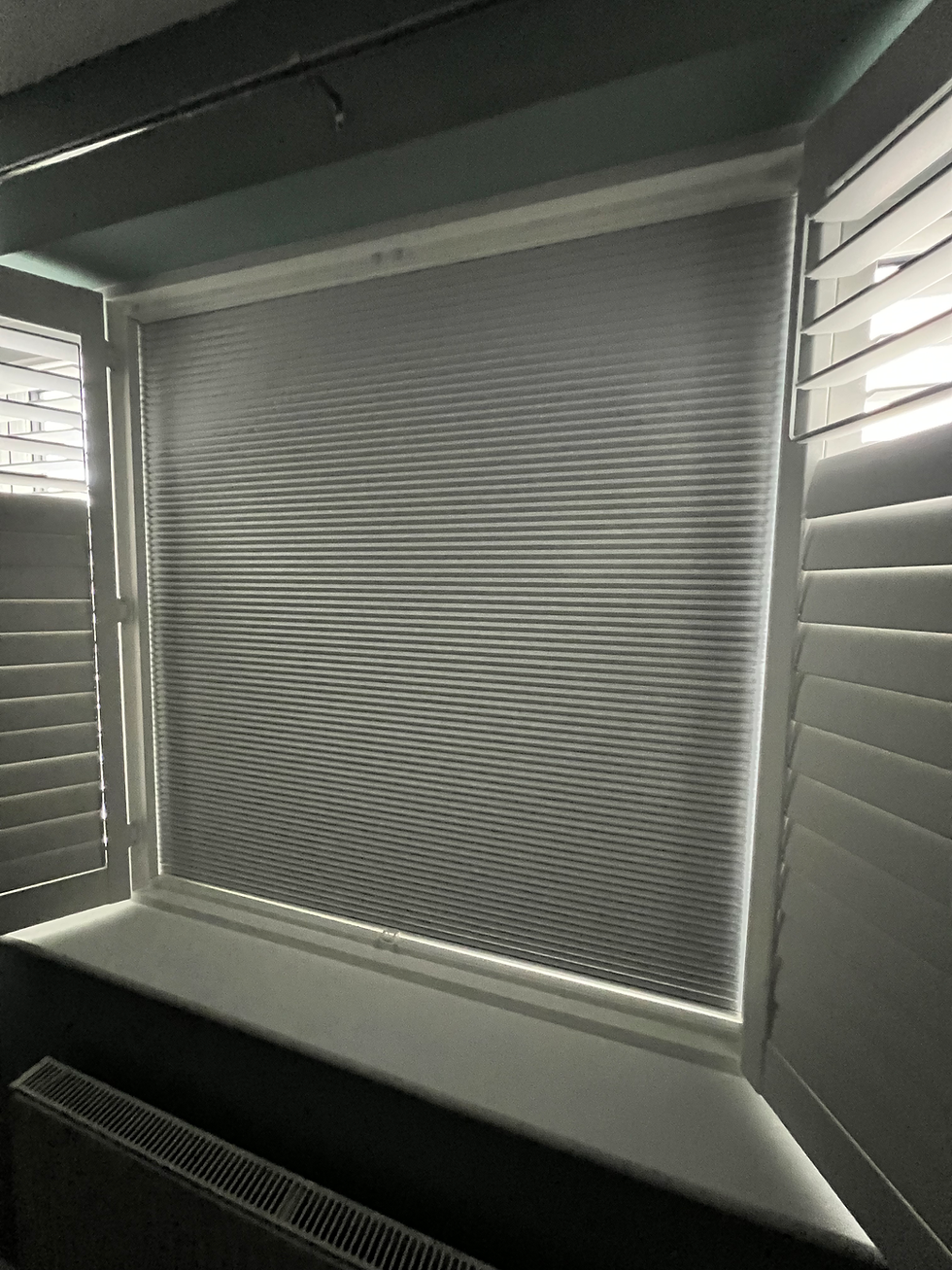 Window fitted with grey pleated blind surrounded by open white plantation shutters