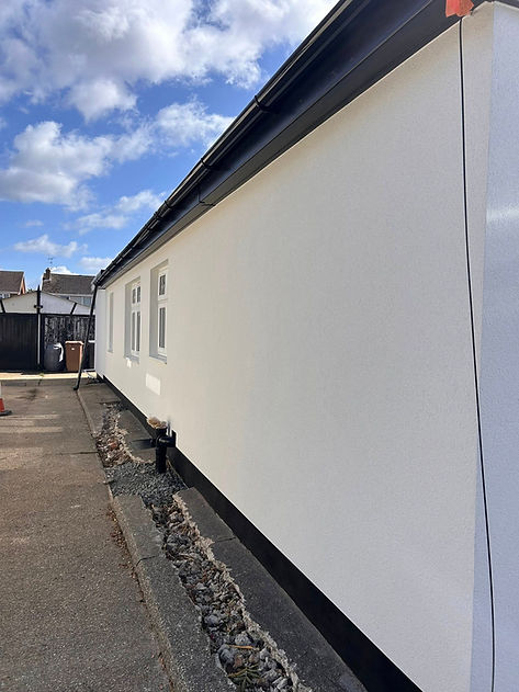 Side view of a white building with three windows, black trim, and a paved path alongside