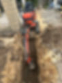 A red excavator arm digs a narrow trench in brown and rocky soil