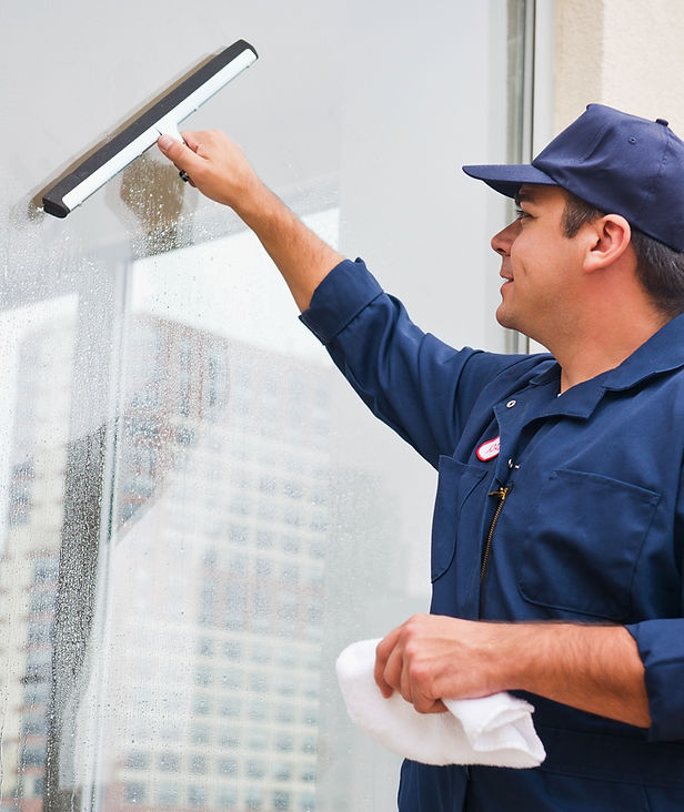 A person in a blue uniform is cleaning a window with a squeegee