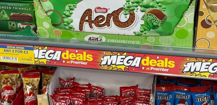 Supermarket shelf displaying Aero, KitKat, and Smarties chocolates with bright mega deals signs