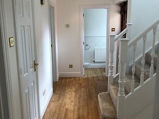 A tidy hallway with wooden flooring leads to a bright bathroom