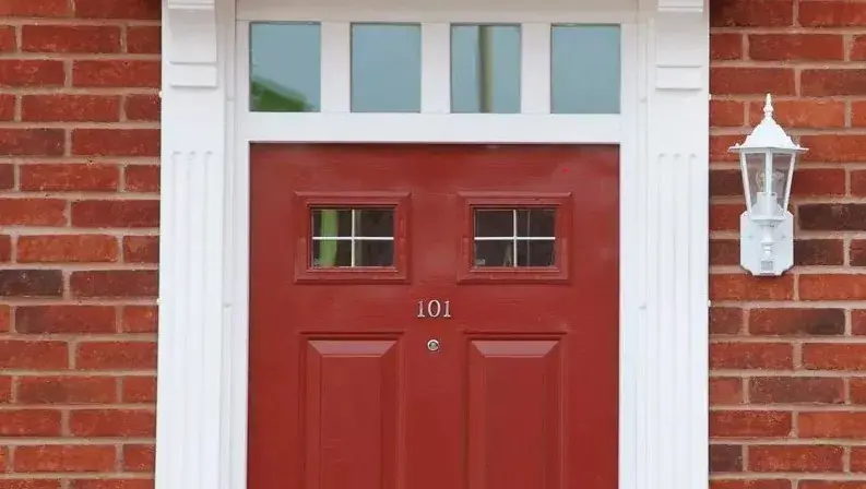 Red front door with two small windows, number 101, set in a brick wall