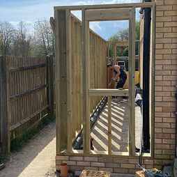 A person is assembling a wooden frame next to a brick house