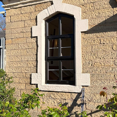 A sunlit stone building with a black-framed, arch-shaped window outlined in white