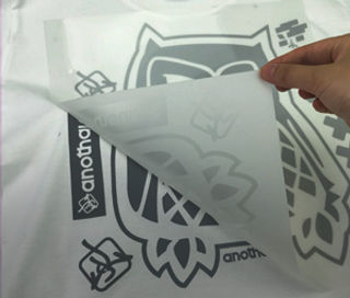 A hand lifts a translucent sheet revealing a gray owl design on a white surface