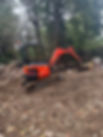 A small orange excavator sits idle on a construction site, surrounded by rubble and debris