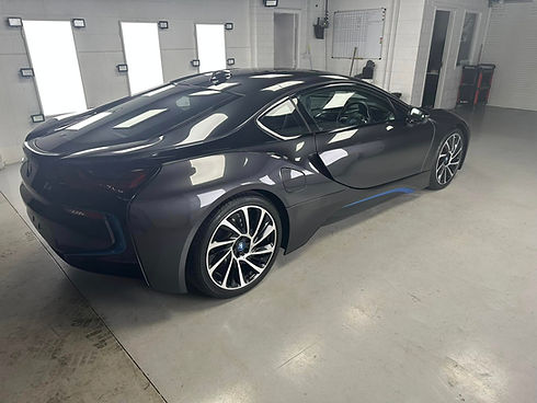 Rear three quarter view of a high gloss grey BMW i8 supercar parked inside a professional detailing bay