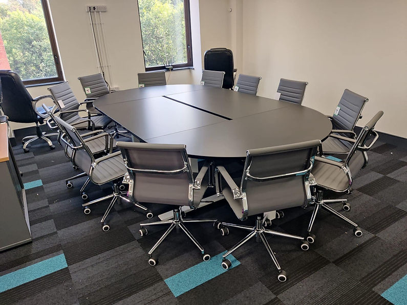 A large, oval conference table with sleek, modern swivel chairs surrounding it in a brightly lit office room