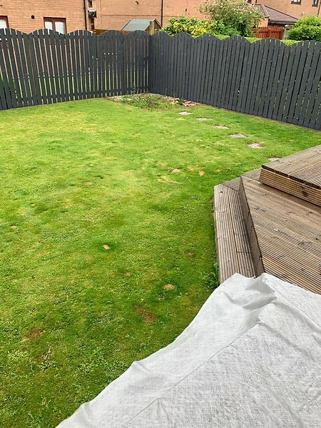 Domestic rear garden showing a lawn with stepping stones, corner timber decking, and a grey fence