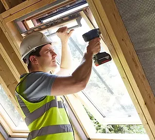 A construction worker in a hard hat and reflective vest uses a power drill to install a window