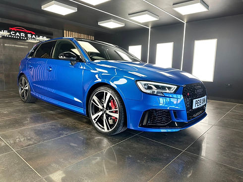 Side profile of a shiny blue Audi hatchback inside a well lit detailing studio