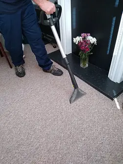 A person is using a carpet cleaning machine on a beige carpet