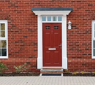 Red door with white frame on brick house, featuring a silver handle and mail slot