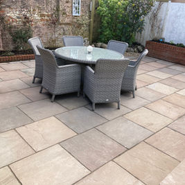 Grey rattan dining table set on spacious stone patio with brick garden wall