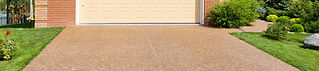 A close-up of a clean, aggregate driveway in front of a beige garage doo